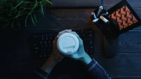 Overhead shot of man drinking coffee and warming up his fingers before typing on Stock Footage 81165602