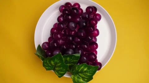 Overhead shot red grape in white plate spinning on yellow background Stock Footage 274041644