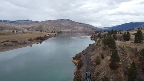 Overhead shot of train passing along a wide river with rolling hills in the d Stock Footage 125054154