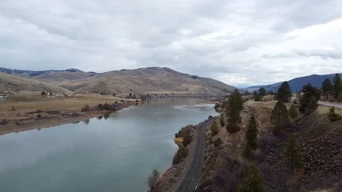 Overhead shot of train track running along a wide river with rolling hills in Stock Footage 125054156