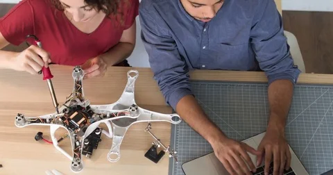 Overhead Tracking Shot Of Man and Woman Wiring A Robot In The Technology Startup Stock Footage 82671672