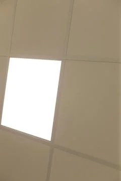 Overhead view of beige office ceiling panels with bright recessed light panel Stock Photos