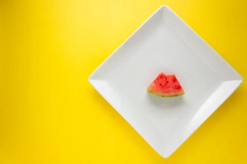 Overhead view bitten slice of watermelon on a white plate. Yellow background. Stock-Fotos
