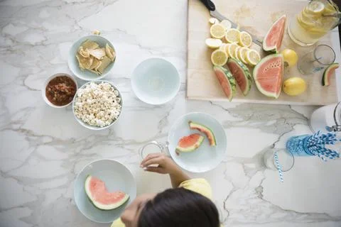 Overhead view boy snacking, eating watermelon and popcorn at kitchen counter Stock Photos