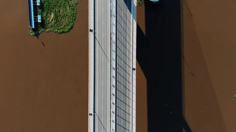 Overhead view captures a concrete bridge spanning brown water 스톡 사진