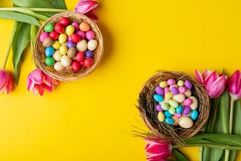 Overhead view of colorful easter eggs and candies in nests with tulips on yellow 스톡 사진