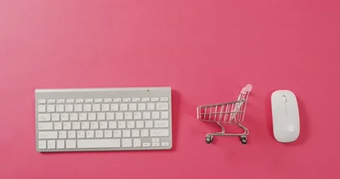 Overhead view of computer keyboard, shopping trolley and mouse on pink Stockbeeldmateriaal 209880995