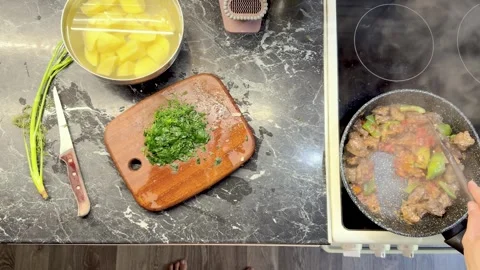 Overhead view of cook stirring meat and vegetable stew beside chopped parsley 스톡 동영상 344631120