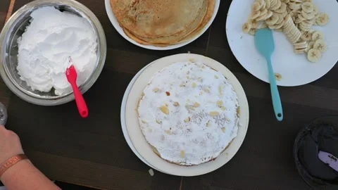 Overhead view of crepe cake topped with whipped cream and almond slices, hands Stock Footage 320681684