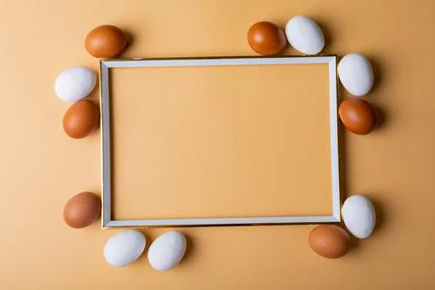 Overhead view of easter eggs around empty frame on orange background with copy Foto stock
