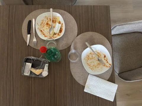 Overhead view of empty dinner plates, cheese, grater, utensils, glasses. Stock Photos