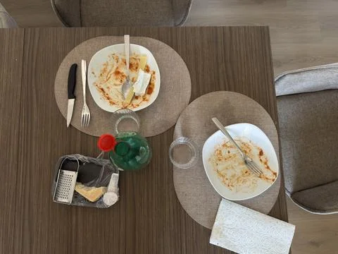 Overhead view of empty dinner plates, cheese, grater, utensils, glasses. Stock Photos