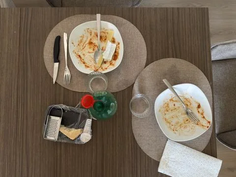 Overhead view of empty dinner plates, cheese, grater, utensils, glasses. Stock Photos