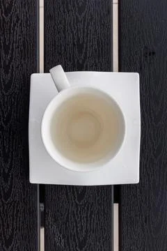 Overhead view of an empty white cup on a square white saucer placed on a da.. Фото