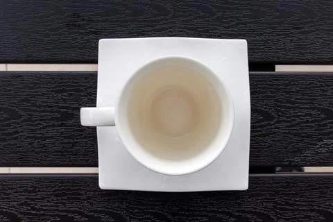 Overhead view of an empty white cup on a square white saucer placed on a da.. Фото