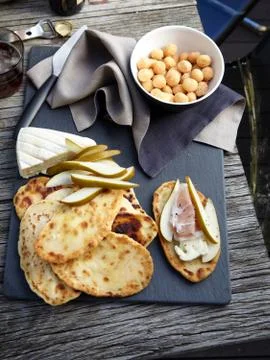 Overhead view of flat breads, taleggio, sliced pears, prosciutto and macadamias Stock Photos