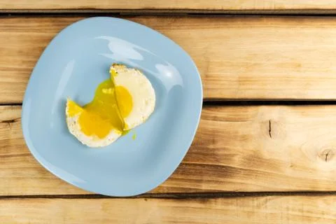 An overhead view of a fried egg cut in half, flowing yolk onto a blue plate. Foto stock