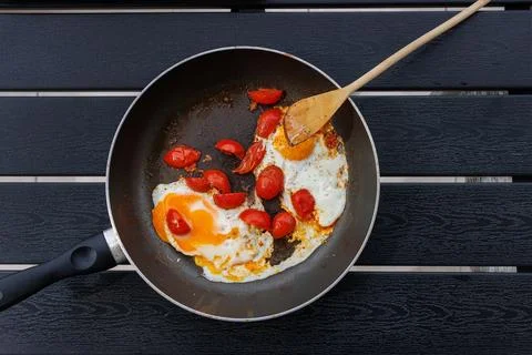 Overhead view of fried eggs cooked with cherry tomatoes in a frying pan on .. Stock Photos