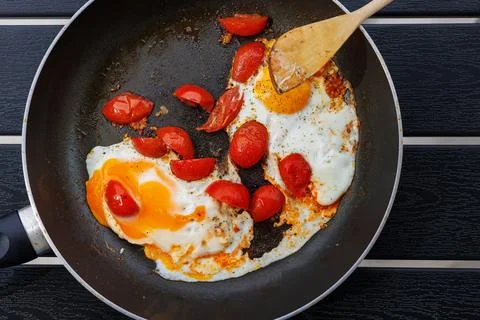 Overhead view of fried eggs cooked with cherry tomatoes in a frying pan on .. Stock Photos