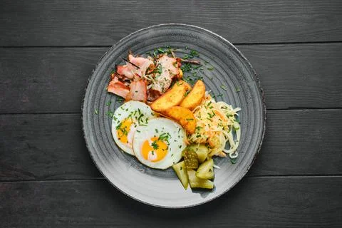 Overhead view of fried eggs, ham with potato wedges, pickled cabbage and cucu Foto stock