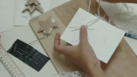 Overhead view of hand sewing white yarn into a star shape pattern on to a thick Stock Footage 311435218