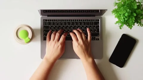 Overhead view of hands typing on a laptop with a plant and phone nearby Stock Footage 337173417