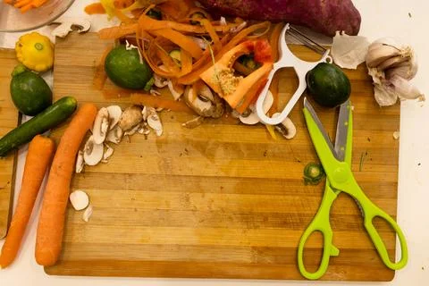 Overhead view of kitchen scissors, peeler and vegetables and peelings on Stock Photos