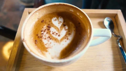 An overhead view of latte with intricate latte art, resting on cafe table. 動画素材 334648694