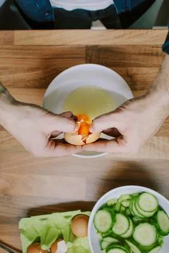 Overhead view of man cracking open an egg to prepare breakfast in the morning Stock Photos