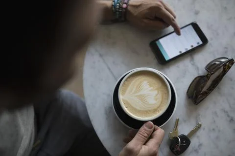 Overhead view man drinking cappuccino with milk foam leaf pattern and using smar Stock Photos