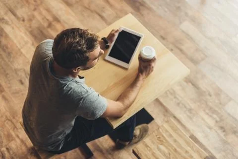 Overhead view of man sitting at table with coffee to go and tablet in cafe 库存照片