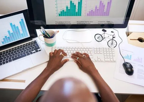 An overhead view of man typing report with graphs at desk with two screens Stock Photos