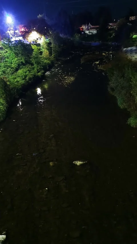 Overhead view of night river with illuminated town buildings distance. Aerial Stock Footage 324927990