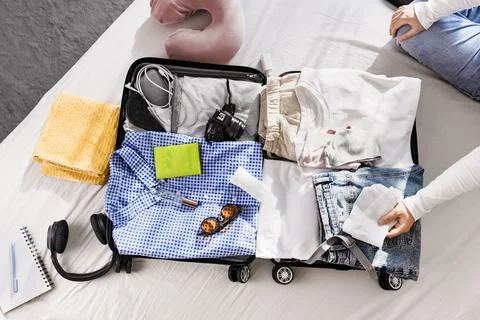 Overhead view of an open suitcase on a bed being packed with clothes, passp.. Stock Photos