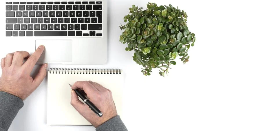 Overhead view of person taking notes on notepad white working on laptop computer Stock Photos