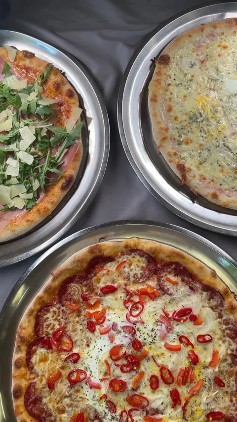 Overhead view of plated artisan pizzas on stainless trays with soft highlights 库存影片 341661723