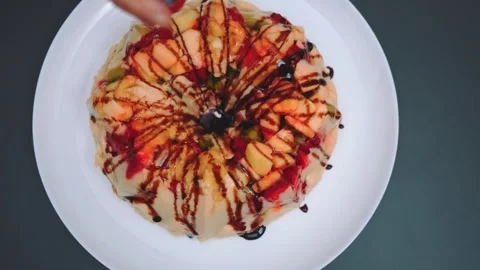 Overhead view of pouring chocolate sauce on fruit-topped soufflé cake Stockbeeldmateriaal 342874535