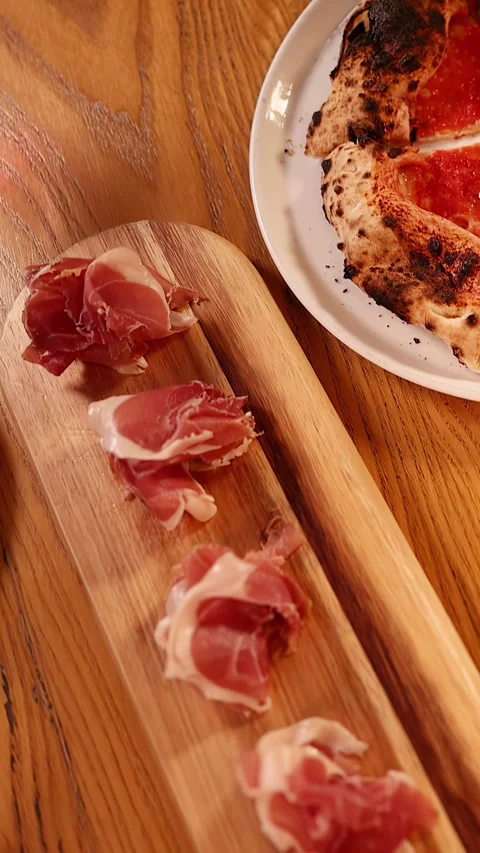 Overhead View of Prosciutto Platter and Neapolitan Pizza on Wooden Table Stock Footage 339518569