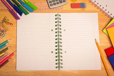 Overhead view is showing open spiral-bound notebook on wooden desk with pens, Stock Illustration