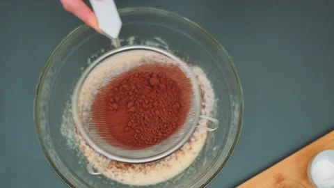 Overhead view of sifting cocoa powder into glass mixing bowl indoors Vidéo 342884780