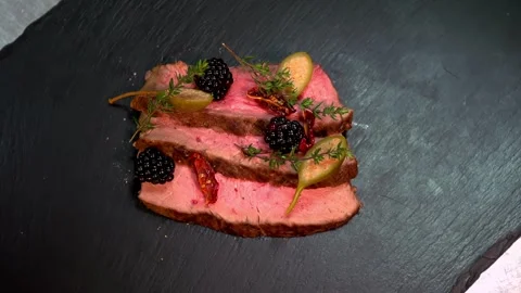 Overhead view of sliced roast beef being seasoned on black slate plate with Stock Footage 332923424