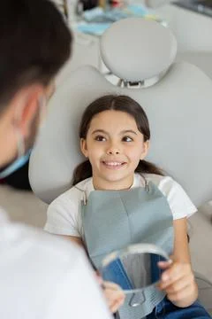 Overhead view of smiling small client sitting in dental chair and holding in  Stock Photos
