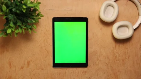 Overhead view of a tablet with a green screen and headphones on a wooden desk Vidéo 341737578