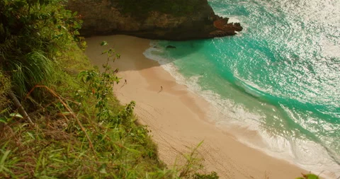 Overhead view of turquoise ocean waves hitting white sand of Kelingking beach in Stock Footage 343379222