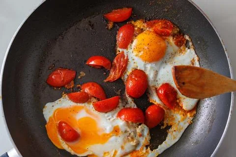 Overhead view of two fried eggs cooked with cherry tomato pieces in a dark .. Stock Photos