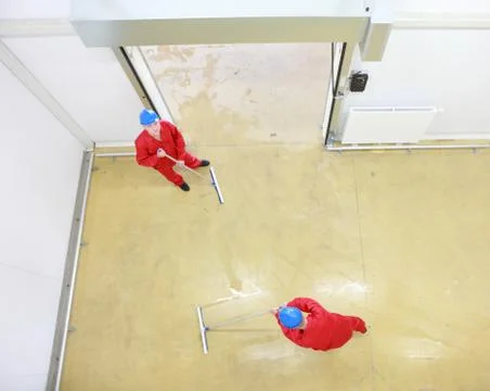 Overhead view of two workers in uniforms  cleaning floor in industrial building Stock Photos