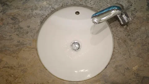 Overhead view of water flowing from shiny chrome faucet into round white si.. Video stock 331719583