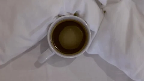 Overhead view of a white cup filled with black coffee on white bed sheets Stock Footage 309059981