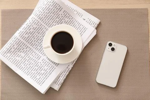 Overhead view of a white smartphone, coffee cup, and newspaper on a textured  Stock Photos