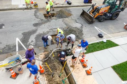 Overhead view of workmen looking into a hole and digging a trench to replac.. Stock Photos